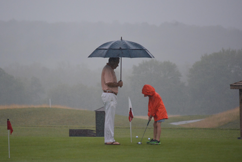 A man and young child on a golf course in the rain
